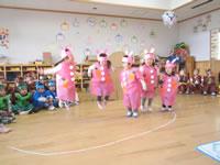 発表会でピンクの衣装をきた園児が踊っているのを他の園児がすわってみている写真