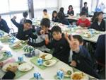 ランチルームで給食をたべている生徒4人がカメラにむかってピースサインをしている写真