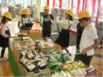 スーパーの野菜売り場で黄色の帽子をかぶった生徒達がたち話をしている写真