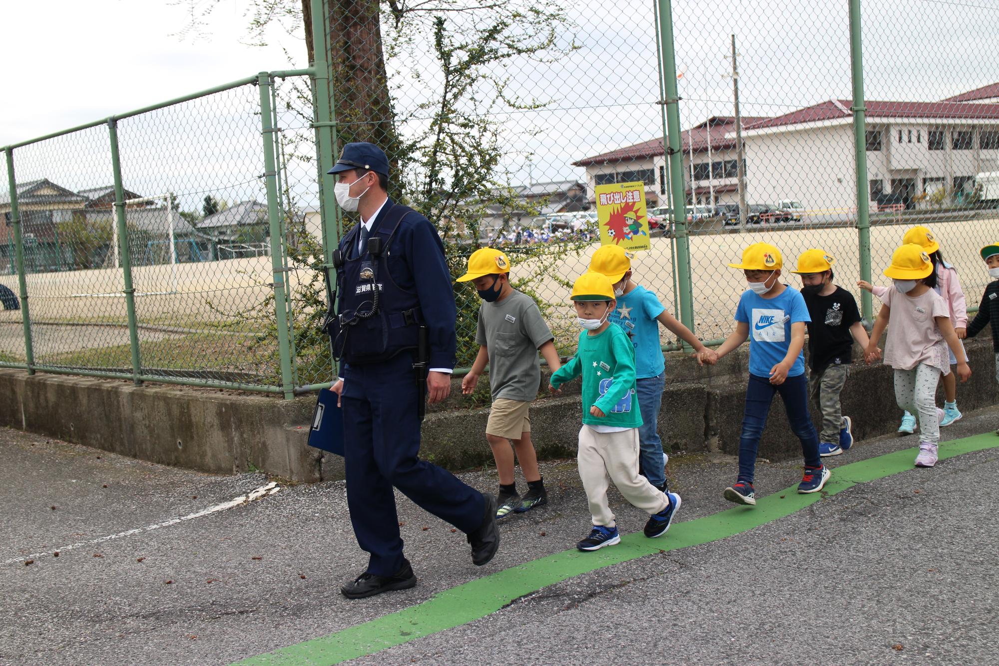 駐在さんを先頭に道路の端を歩く一年生