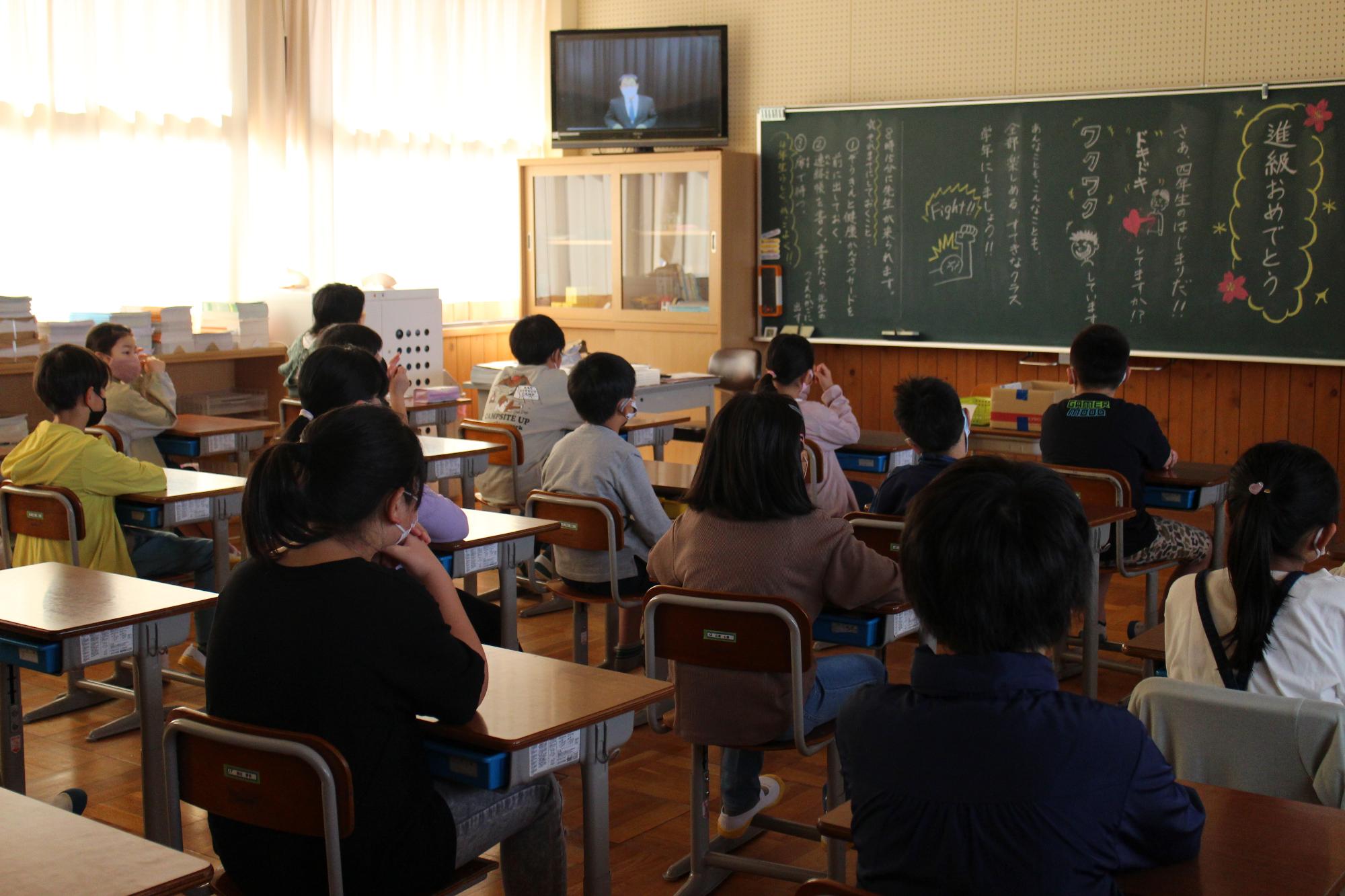 教室でテレビ画面の校長先生の話を聞く子供たち