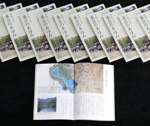 秦荘のあゆみの冊子が10冊並べて置いてある下に冊子を開いた状態で1冊置いてある写真