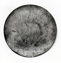 丸い鋳銅鏡板の表面に千手観音坐像を線刻した写真