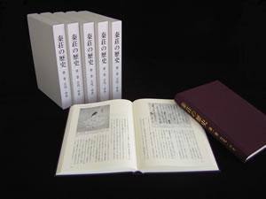 5冊立てて置いてあり手前に1冊閉じたままもう1冊は開いて置いてある『秦荘の歴史』第一巻 古代・近世編の写真