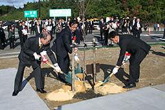 3名の男性がスコップで開通記念植樹をしている写真