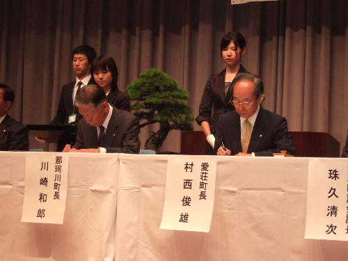 愛荘町と那珂川町の姉妹都市提携盟約式で両町長が盟約書と災害時相互応援協定書に署名している写真